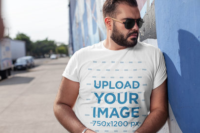 Plus Size T-Shirt Mockup of a Man with Dark Glasses Leaning on Blue Wall