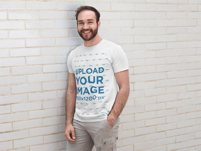 T-Shirt Mockup of a Young Man Leaning Against a White Wall 