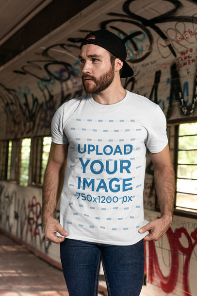 T-Shirt Mockup Featuring a Bearded Man with a Cap by a Graffiti Wall