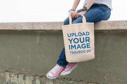 Tote Bag Mockup Featuring a Young Woman Sitting on a Wall