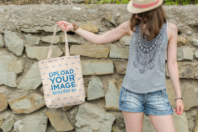 Mockup of a Woman Holding a Canvas Tote Bag Mockup Against a Rocky Wall