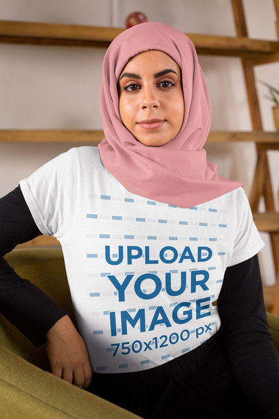 T-Shirt Mockup Featuring a Woman with a Hijab Sitting on a Sofa 