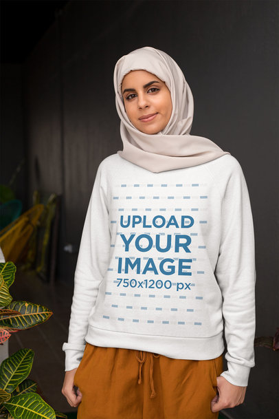 Sweatshirt Mockup of a Woman Wearing a Hijab Standing Next to a Plant