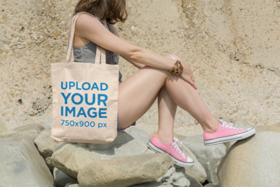 Tote Bag Mockup of a Young Woman Sitting on Rocks in a Sunny Day