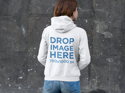 Woman Wearing a Pullover Hoodie Mockup Standing in Front of a Wall