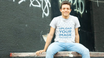 T-Shirt Video of a Man Sitting on a Wooden Platform Against a Graffiti Wall 
