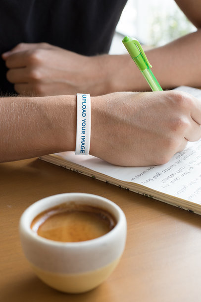 Silicone Wristband Mockup Featuring a Man Writing at a Cafe 
