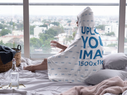 Mockup of a Woman Wearing a Hooded Fleece Blanket and Looking out the Window