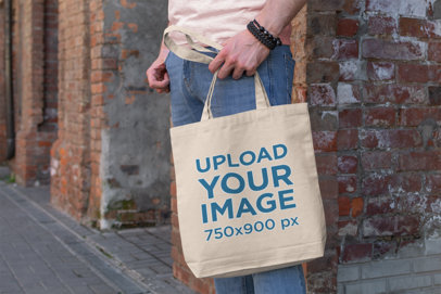 Mockup of a Man Holding a Tote Bag Next to a Brick Wall 192-el