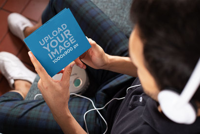 Mockup of a Man Holding a Digipak While Listening to Music