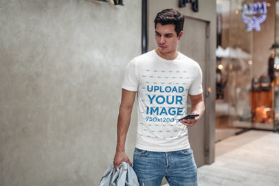T-Shirt Mockup Featuring a Young Man by a Store Checking His Phone