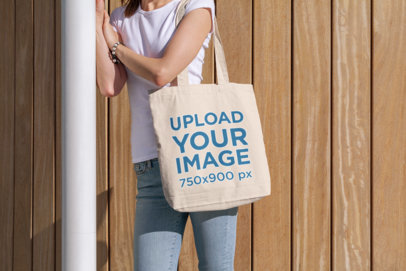 Tote Bag Mockup Featuring a Young Woman Standing by a Wooden Wall 