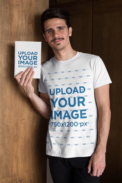 T-Shirt Mockup of a Man Holding a Book While Leaning on a Wooden Door