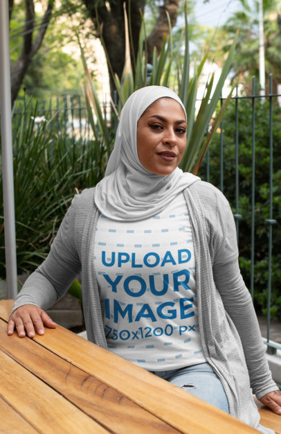 T-Shirt Mockup Featuring a Woman in a Hijab Sitting at a Table