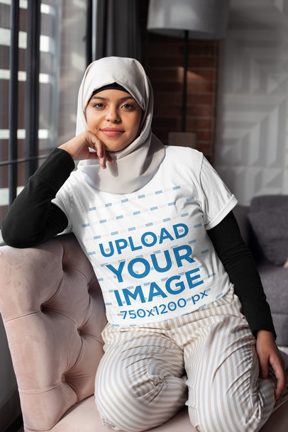 T-Shirt Mockup of a Woman in a Hijab Sitting on a Couch 