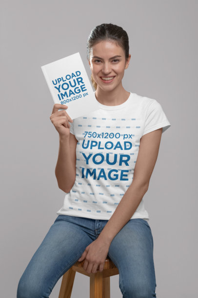 Mockup of a Woman Wearing a T-Shirt and Holding a Book at a Studio