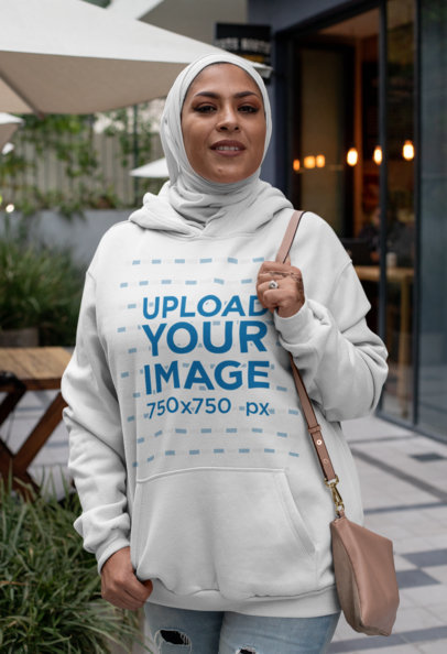 Hoodie Mockup Featuring a Woman with a Hijab Outside a Restaurant 