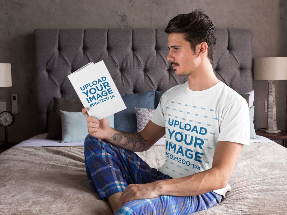 T-Shirt Mockup Featuring a Tattooed Man Reading in His Bedroom 