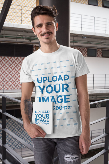 T-Shirt Mockup of a Man Holding a Book at a Building's Hallway 