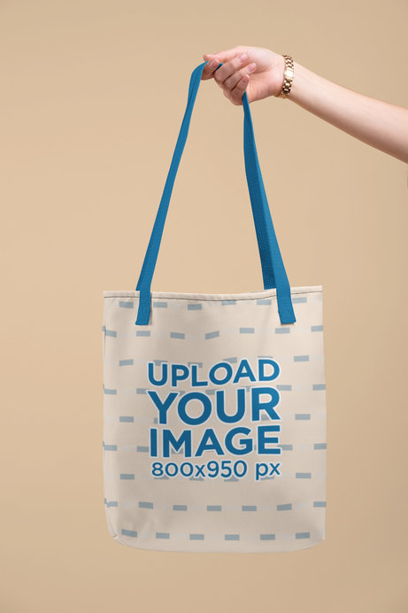 Mockup of a Hand Holding a Customizable Strap Tote Bag Against a Flat Surface 
