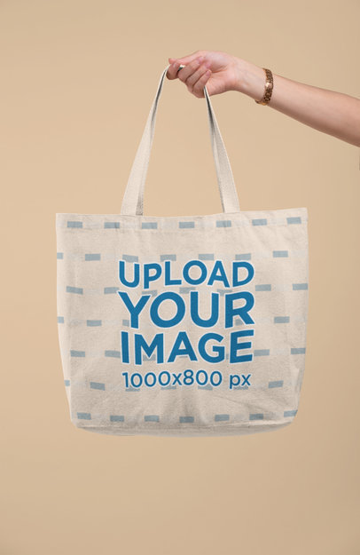 Mockup of a Hand Holding a Tote Bag Against a Solid Color Background 