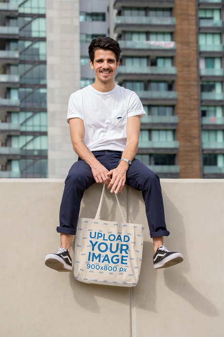 Tote Bag Mockup Featuring a Stylish Man Sitting on a Wall 