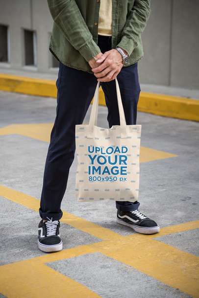 Mockup of a Man Holding a Tote Bag on a Painted Street 