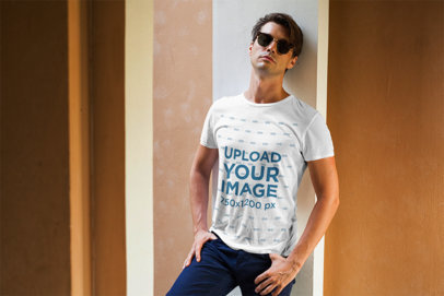 T-Shirt Mockup Featuring a Stylish Man With Sunglasses Leaning Against a Wall