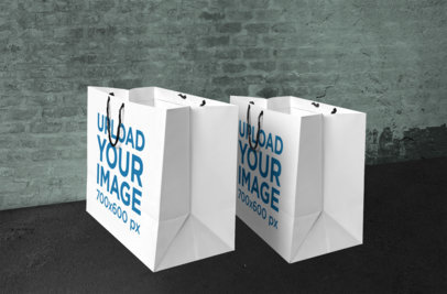 Mockup of Two Paper Shopping Bags in Front of a Brick Wall