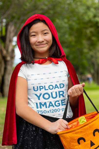 T-Shirt Mockup of a Happy Girl in a Red Coat Holding a Pumpkin Bag