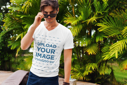 V-Neck T-Shirt Mockup Featuring a Man with Sunglasses Posing Against Some Palm Trees