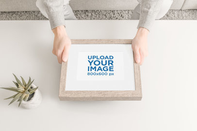Mockup of a Man Holding a Wooden Picture Frame over a Living Room Table
