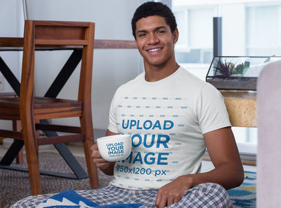T-Shirt Mockup Featuring a Young Man Holding a 24 oz Mug in the Living Room 29255