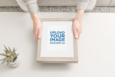 Mockup of Two Hands Holding a Wooden Picture Frame by an Indoor Plant