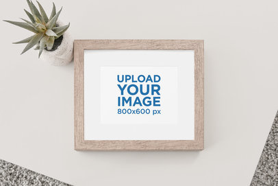 Mockup of a Wooden Picture Frame on a Plain Surface with a Desert Plant