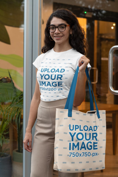 T-Shirt Mockup of a Stylish Woman Holding a Tote Bag with a Customizable Strap 