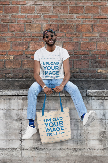 T-Shirt Mockup of a Man with a Tote Bag in Front of an Old Brick Wall