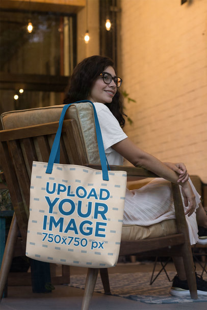 Tote Bag Mockup Featuring a Woman with Glasses Sitting on a Chair