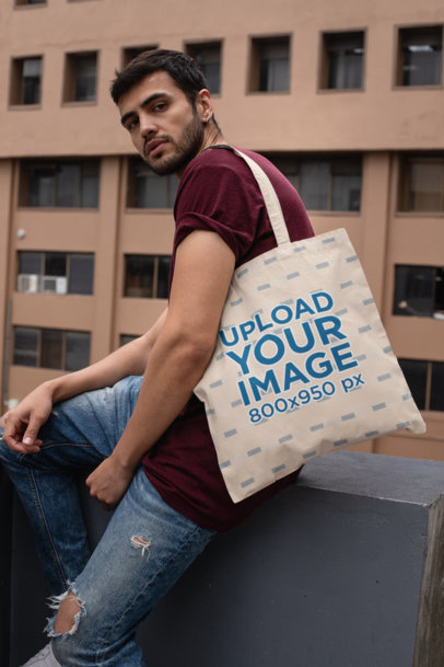 Tote Bag Mockup of a Stylish Man Sitting on a Concrete Fence
