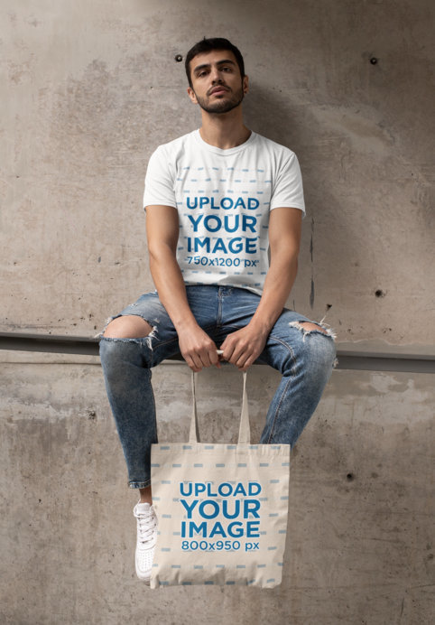 T-Shirt Mockup of a Bearded Man with a Tote Bag Sitting on a Concrete Structure