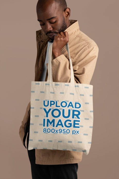 Mockup of a Bald Man Holding a Sublimated Tote Bag at a Studio