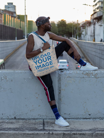 Mockup of a Trendy Man Carrying a Customizable Strap Tote Bag in an Urban Scenery