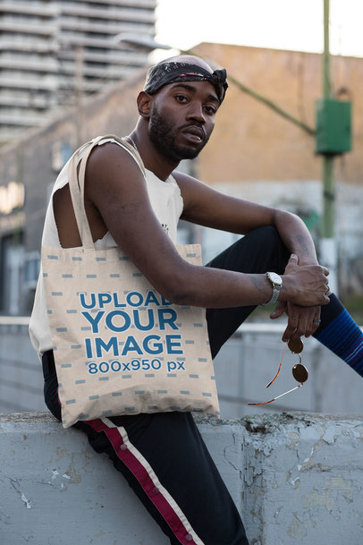 Tote Bag Mockup of a Cool Guy Sitting on a Concrete Fence 