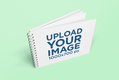 Mockup Featuring a Spiral Notebook Standing Against a Plain Background 