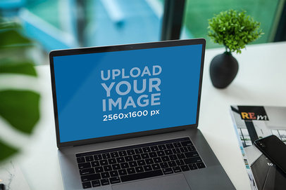 Mockup of a MacBook Pro Placed on a Desk by a Magazine