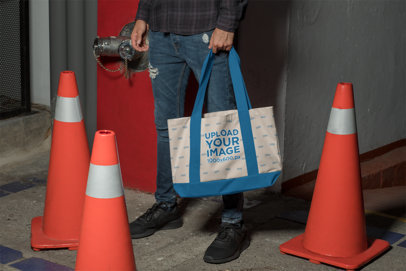 Mockup of a Man Holding a Sublimated Weekend Tote Bag by Traffic Cones