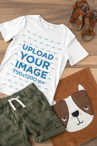 Mockup of a T-Shirt for a Boy Placed on a Wooden Surface with an Outfit