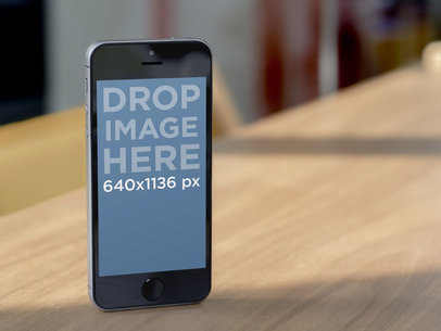 Mockup of a Dark Color iPhone 5 in Portrait Position on a Wooden Table