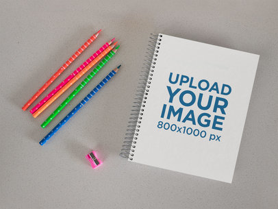 Mockup of a Spiral Notebook Placed by Some Pencils