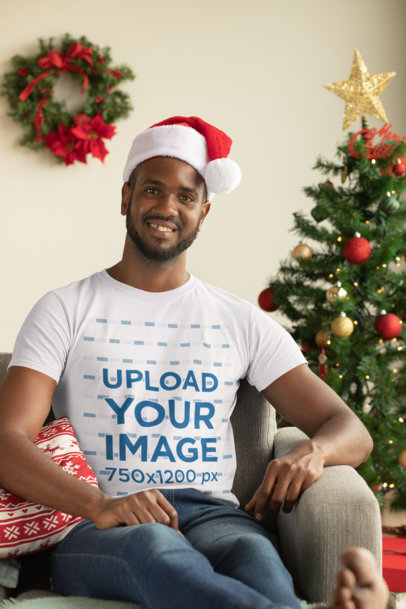 Mockup of a Man with a Crewneck T-Shirt Sitting Next to a Christmas Tree